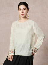 Model wearing a cream white long-sleeve blouse with a round neck and embroidered cuffs, paired with a black pleated skirt, showcasing the elegant silhouette.