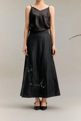 Black silk A-line maxi skirt with green and white abstract embroidery at the hem, crafted from 100% mulberry silk, paired with a black camisole.
