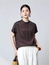 Front view of a dark brown textured silk blouse with a stand collar and short sleeves, styled with white wide-leg trousers, perfect for a chic commuter style.