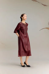 Side profile of a women's burgundy silk midi dress with a relaxed fit, three-quarter sleeves, and embroidered cuffs, styled with black heels for an elegant look.