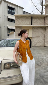 Model leaning on a cream car in a rust brown mandarin collar vest, holding a woven bag, highlighting the 88% viscose and 12% nylon fabric.