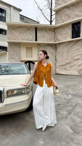 Front view of a women's button-down sleeveless Qipao top in deep caramel brown, paired with wide-leg white trousers and white shoes.