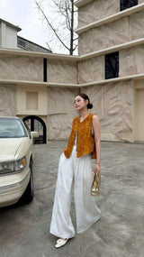 Full body shot of a New Chinese style sleeveless vest top in amber brown, worn over white pants, showcasing a vintage aesthetic and elegant drape.