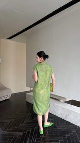 Back view of a sage green Cheongsam dress with a sleeveless design and textured fabric, paired with green heels and a matching bag.