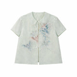 Flat lay of a light green short-sleeve top with a Peter Pan collar and delicate butterfly & floral embroidery, featuring a front button closure.