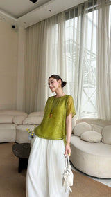 Side view of a woman wearing a bright green blouse with short sleeves and a round neck, holding a white handbag, showcasing the elegant drape.