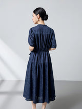 Back view of a navy blue silk jacquard dress with a tie waist and gathered tiers, showcasing the beautiful drape and subtle sheen of the premium silk.