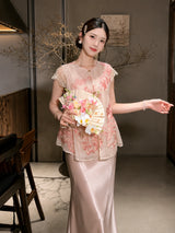 Front view of a pink sheer embroidered vest with a ruffled hem, styled with a matching satin skirt and holding a floral fan.
