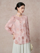 Model wearing a pink sheer silk blouse with an ancient pottery cutwork pattern and a matching necktie, paired with a cream skirt.