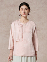 Front view of a women's pink silk blouse with a round neckline and a delicate diagonal placket with decorative tassels and beads.