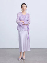 Model wearing a light purple New Chinese style cardigan with a V-neckline, butterfly embroidery, and front buttons, paired with a matching silk skirt, holding a beaded tassel accessory.