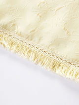 Close-up of the textured jacquard fabric and delicate fringe tassel hem on a cream yellow silk blouse.