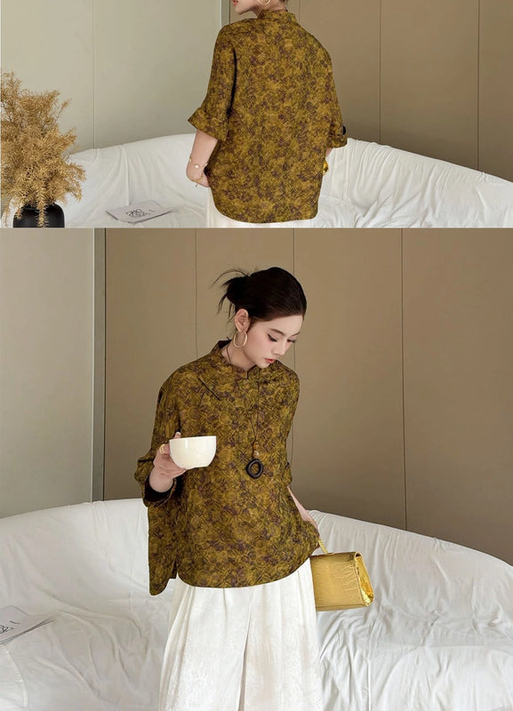 Model wearing The Silk Co olive floral print blouse with white wide-leg trousers and gold accessories