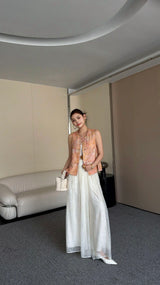Woman wearing a sleeveless vintage Cheongsam vest top with pink and gold brocade floral pattern, paired with white wide-leg pants and white bag.