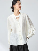 Model wearing a white long-sleeve jacquard blouse with a stand collar, featuring a relaxed fit and subtle floral pattern, perfect for a refined New Chinese look.