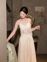 Model wearing a white lace camisole with spaghetti straps, layered under a pleated skirt, showcasing the elegant V-neckline and scalloped hem.