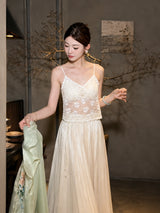 Front view of a model wearing a white lace camisole with a V-neckline and scalloped hem, holding a green garment, styled for a delicate and feminine look.