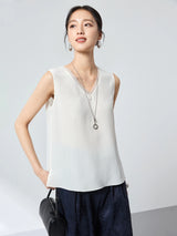 Front view of a women's white V-neck sleeveless vest with a relaxed A-line silhouette, paired with dark blue pants and a black handbag.