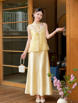 Front view of a yellow embroidered Cheongsam vest with pearl buttons and a matching satin skirt, holding a white beaded handbag, 100% polyester.