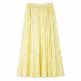 Flat lay of a yellow shiny pleated maxi skirt with elastic waistband and side tassel tie, crafted from 100% polyester.