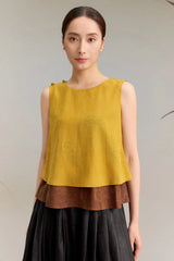 Close-up of a yellow silk top with a double-layered hem and button details on the shoulder, highlighting the textured jacquard finish and the luxurious silk material.